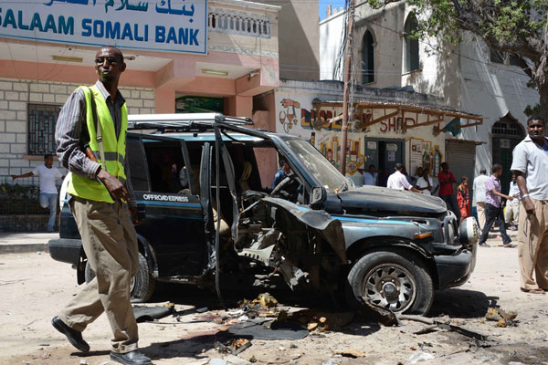 An armed man stands in front of the remains of the car in which a Somali lawmaker was assassinated and another wounded on April 21, 2014, in Mogadishu, in the latest in a series of bomb attacks in the war-ravaged capital. AFP PHOTO / MOHAMED ABDIWAHAB