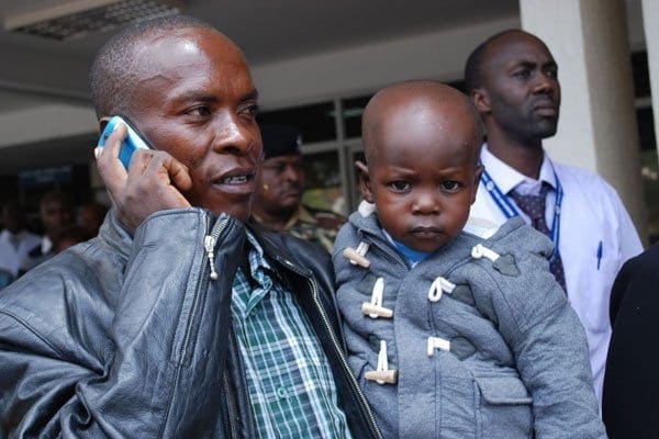 Benson Osinya (on phone) with his son Satrine Osinya outside Kenyatta National Hospital, Nairobi on April 10, 2014 soon after the young Osinya was discharged. DENISH OCHIENG