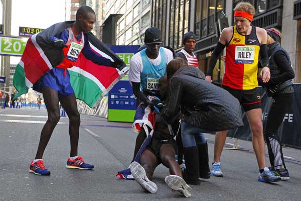Mo Farah of Great Britain collapses at the finish line in the arms of Stephen Sambu of Kenya (C) and his wife Tania, as Geoffrey Mutai of Kenya (L) looks on at the 2014 New York City Half Marathon in lower Manhattan on March 16, 2014 in New York City. Mutai won as Farah finished second and Mutai in third. PHOTO/AFP
